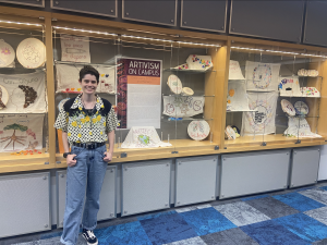 Rooke Breede, a graphic design student, stands by the display case she designed for the Embroidery for Peace and Memory event. 
